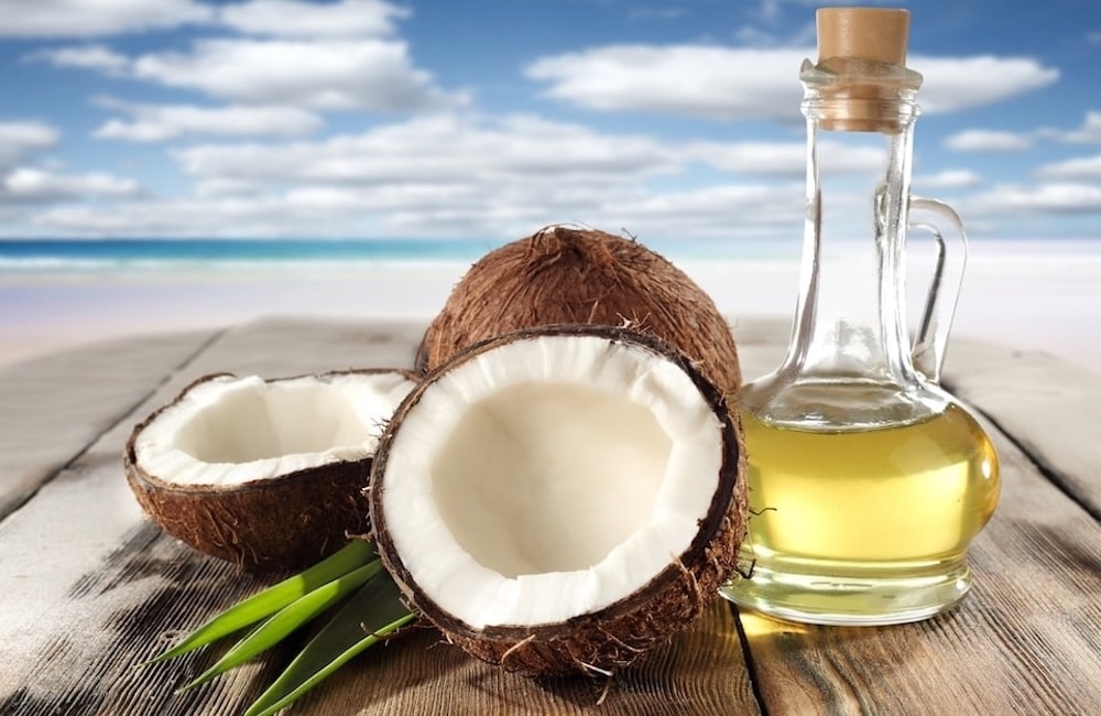 Coconut and Oil bottle on table. Beach in the background